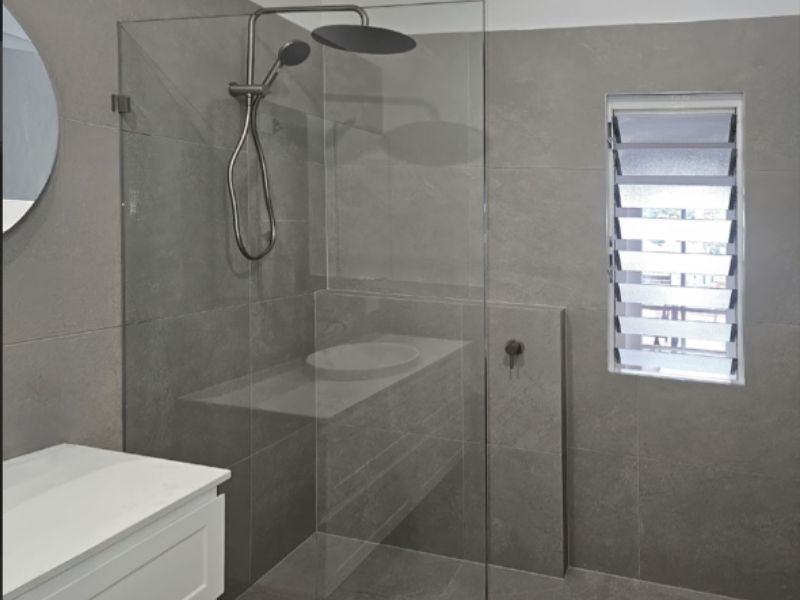 Grey tiled bathroom with frameless glass panel and black fittings, displaying different types of shower screens.