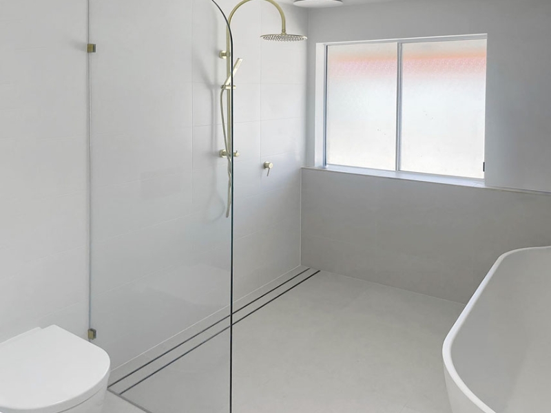 Modern bathroom with frameless glass panel installed beside a toilet, showing a minimalist layout suitable for a standard shower screen size.